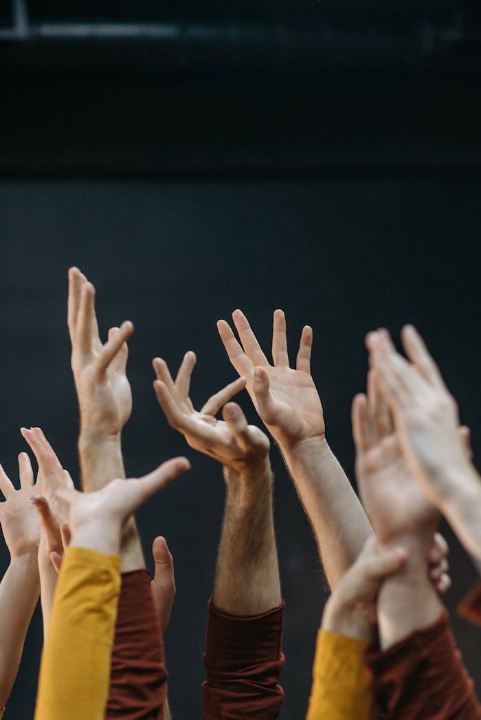 A collection of raised human hands in unity and diversity against a dark background.